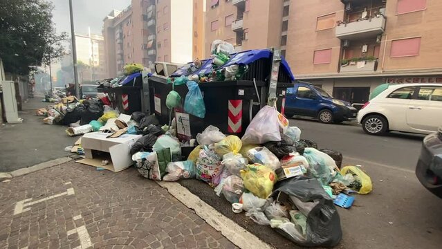 Awful scene of Roman street full of abandoned trash on sidewalk near the residential buildings, overfilled garbage containers under the buildings open windows, lack of street cleaning in the capital