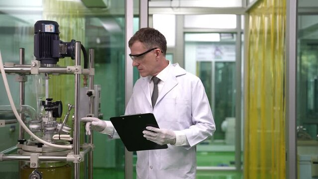 Maintenance service engineer holding paper holder chart check list checking the glass tube syphon information at canabis distillation plant before start up operation 
