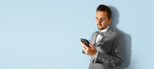 Young businessman using smartphone in a suit on a light blue background