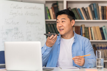 Asian Male Tutor Using Voice Search Application Sitting At Workplace