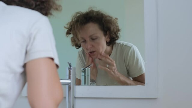 A tired woman in the morning washes her face with cold water in order to wake up and refresh herself. Daily routine in the bathroom, sleepy woman washing her face and looking at herself.