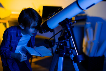 Boy carefully looks through a telescope. Smart inquisitive child explores sky through on a summer day with space maps on background. Cosmos and universe, Milky way stars. My astronomy science work
