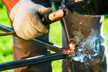 Selective focus on the hot tip of the electrode during operation of the electric arc welding machine. Sparks and smoke during the burning of metal.