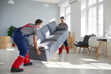 Two young workers lift up heavy sofa together. Young men from moving company and lorry delivery...