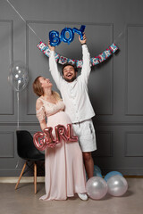 Full length view of a amused couple holding up inscription boy or girl during gender reveals party, over balloons.