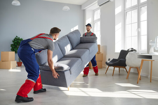 Two young workers lift up heavy sofa together. Young men from moving company and lorry delivery service removing things from the house, carrying furniture and other belongings