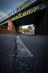 Fototapeta na wymiar Abstract artistic shot of a railway bridge with low bridge sign over a road
