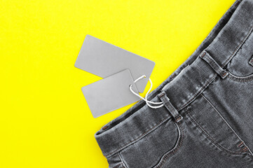 Flat lay, detail of black jeans, blank grey labels on yellow background.
