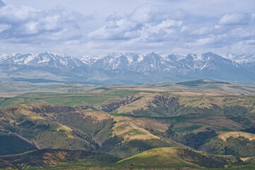 Atmospheric alpine landscape with mountain range and green hills under dramatic cloudy sky. Beautiful highland scenery.