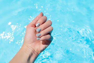 Female hand with vacation nail design. Glitter aquamarine nail polish manicure. Female hand on a...