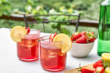 Fresh summer strawberry cocktail or mocktail on the table in the garden. Sparkling pink strawberry lemonade.