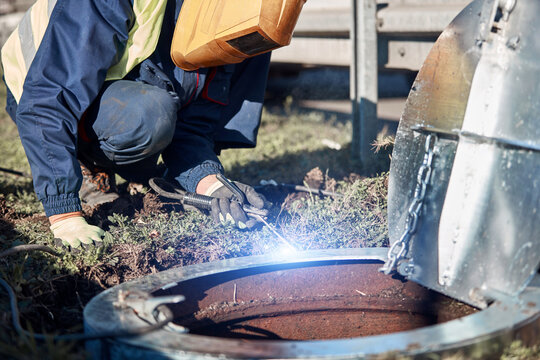 Welder handyman working on a sewer manhole lid.