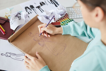 Over shoulder view of fashion designer sitting at table and brainstorming about dress design while drawing sketch