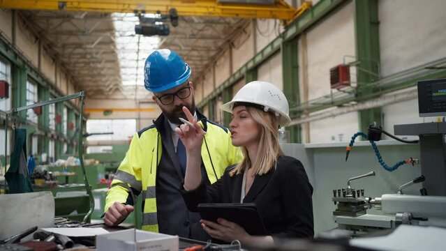 Male and female industrial engineers discussing factory's new machinery project and using tablet.