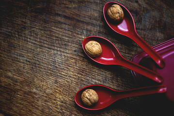 walnuts in red ceramic spoons on a dark gray wooden background