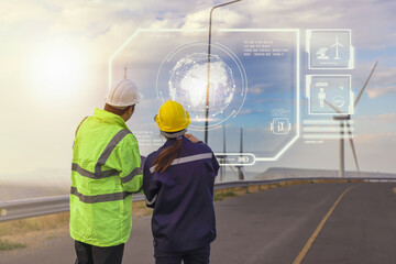 Young maintenance engineer team working in wind turbine farm at sunset on interface data.