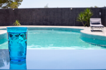 glass of blue water in front of the pool, summer image, pastel colors