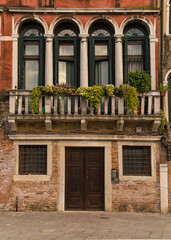 Fototapeta na wymiar Architectural detail of an old charming facade with green plants hanging over in Venice, Italy 