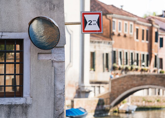 Convex mirror reflecting a canal water, street sign and typical architecture on background in Venice, Italy 