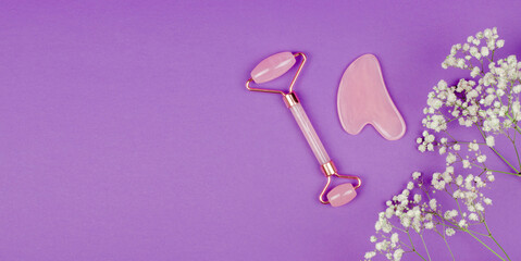 Rose quartz gua sha massage scraper and face massage roller on purple background with gypsophila...