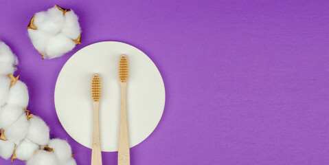 Two wooden toothbrushes and cotton flowers on a purple background. Personal hygiene items