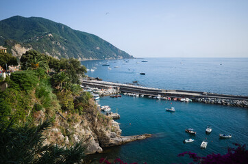 Seascape with long breakwater near marina of Camogli, Liguria, Italy. Mediterranean landscape of Italian Riviera with rocky coastline covered with greenery and palm trees and yachts and boats in bay