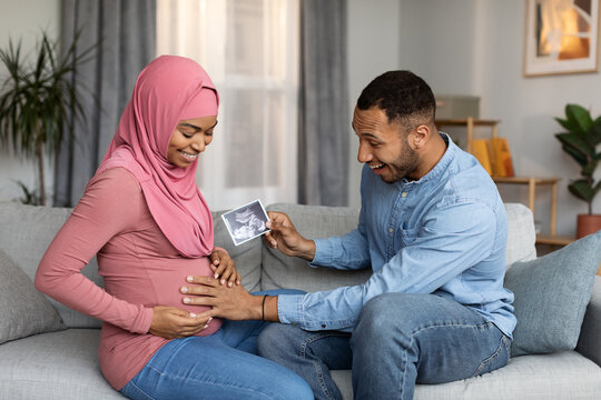 Exited Black Man Holding Baby Sonograph And Touching Pregant Muslim Wife's Belly