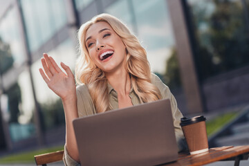 Portrait of attractive cheerful wavy haired girl using netbook waving hi hello waiting friend in complex outdoors