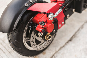 Closeup of a rear wheel, mud guard and disc brake of an electric kick scooter parked by the edge of...