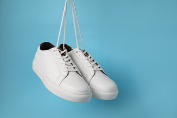 Pair of stylish white sneakers hanging on light blue background, space for text