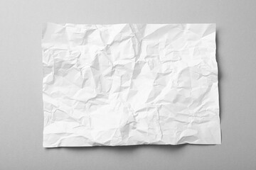 Sheet of white crumpled paper on grey background, top view