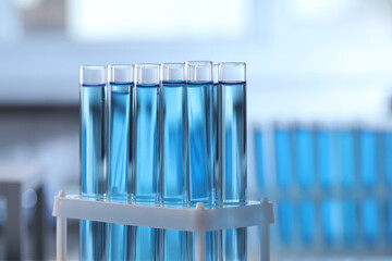 Test tubes with light blue liquid on blurred background, closeup