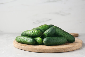 Board with fresh ripe cucumbers on white marble table, space for text