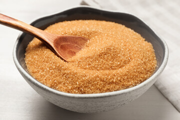 Brown sugar in bowl on white wooden table, closeup