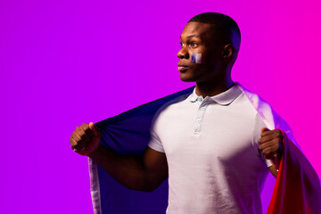 Happy african american male supporter with flag of france over pink lighting