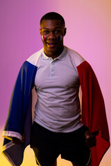 Portrait of happy african american male supporter with flag of france over pink lighting