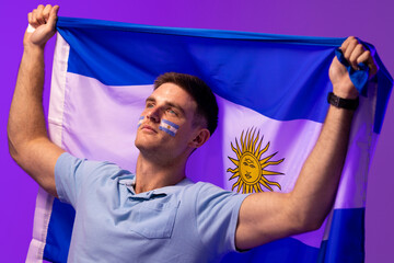 Happy caucasian male supporter with flag of argentina over pink lighting