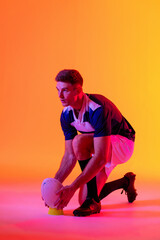 Fototapeta na wymiar Caucasian male rugby player crouching with rugby ball over pink lighting