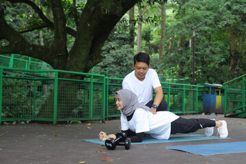 Young Asian man helping his wife doing plank at the park. Healthy lifestyle couple concept.