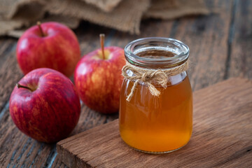 Apple cider vinegar in glass bottle and fresh red apples on wooden table