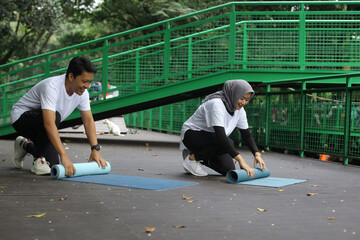 Young Asian couple rolling yoga pilates mat after workput at the park. Healthy lifestyle couple concept.
