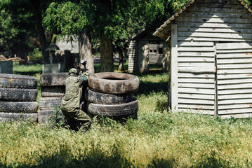 Fototapeta premium Paintball player shooting with marker from behind the tyre cover during the paintball game