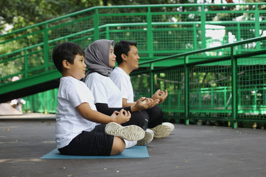  Young Asian family doing exercise in meditate yoga pose together at the greenery park. Healthy lifestyle family concept.