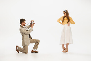 Obraz premium Portrait of young man taking photo of beautiful young women with retro camera isolated over white background
