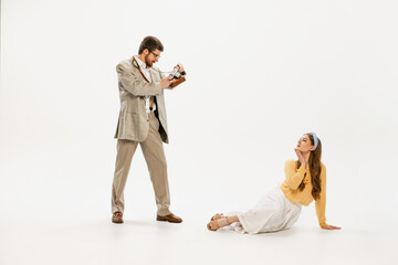 Portrait of young man taking photo of beautiful, stylish, young women with retro camera isolated over white background