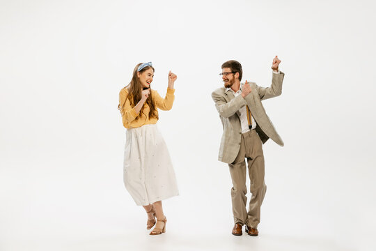 Portrait of cheerful young couple in vintage style outfit dancing, having fun isolated over white studio background. Party time