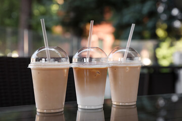 Plastic takeaway cups of delicious iced coffee on table in outdoor cafe