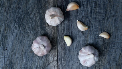 Flat lay perspective of a three garlic cloves on top rustic wood table, captured in the dark mood...