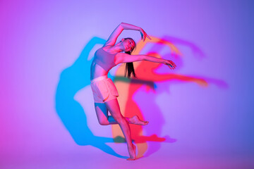 Dancing young girl in sports uniform practicing isolated on gradient studio background in neon...