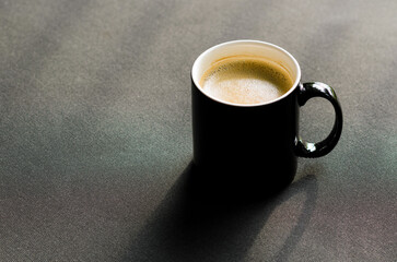 A black cup of hot coffee put on balcony couch with shadow from morning sunshine.